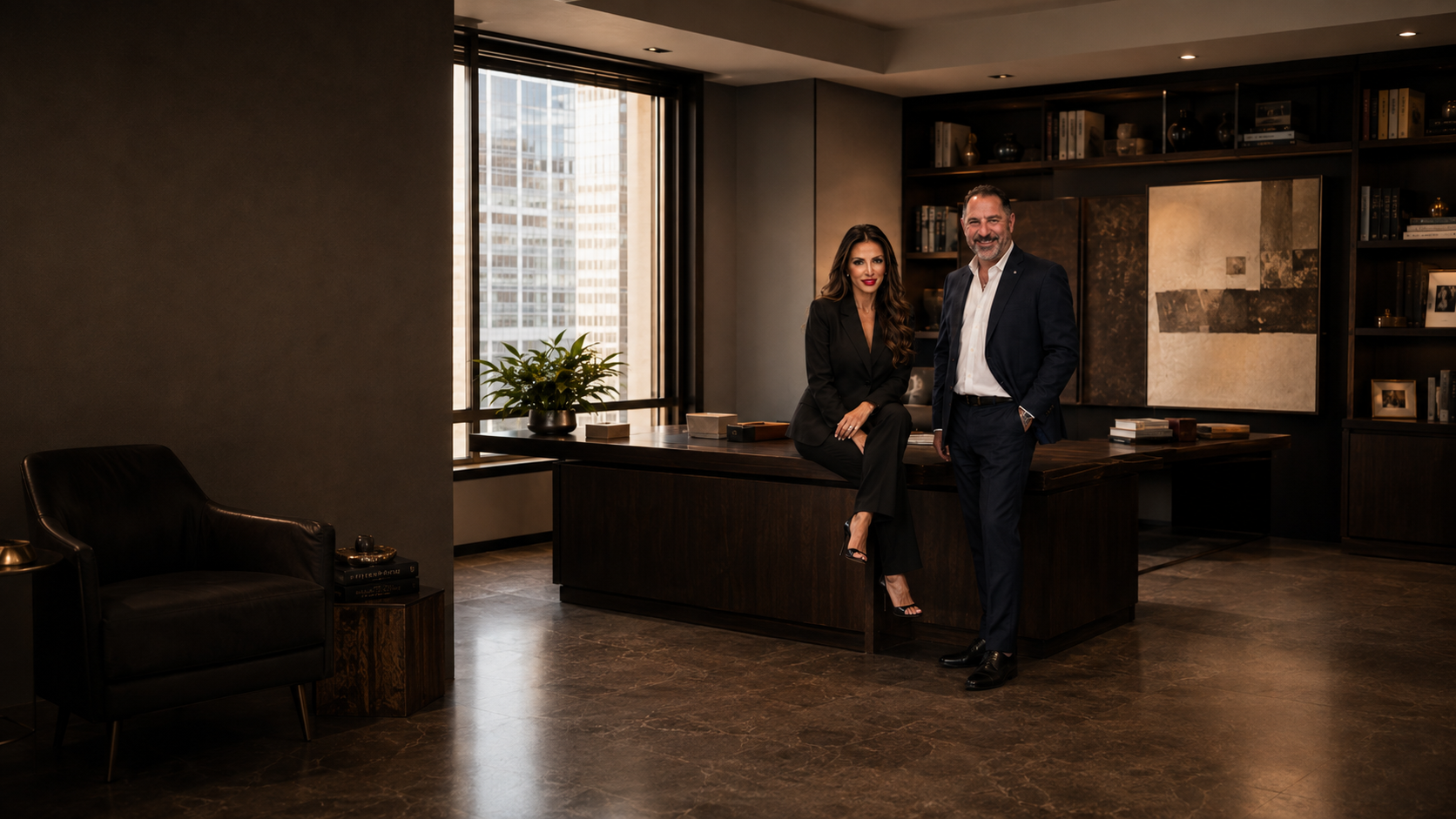 Madeline Ricci and David Ricci in a corner office with a city view behind them, both dressed in black