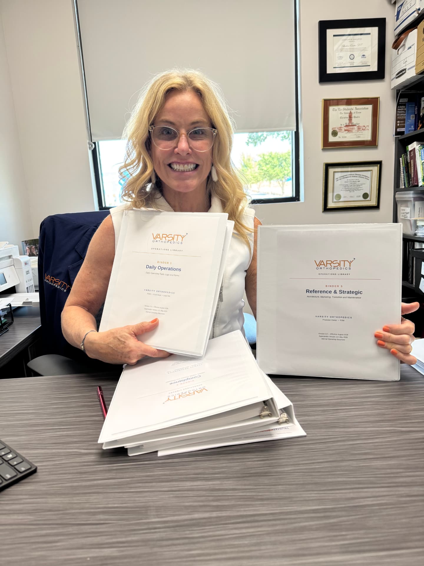 Dr. Quatro Ott at her desk holding two binders from the Varsity Orthopedics operations library